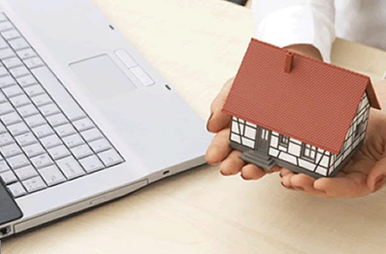 Hands holding a model house besides a laptop