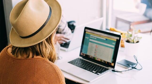 Woman in cowboy hat seated facing a laptop and phone charging on a table - MyPoints